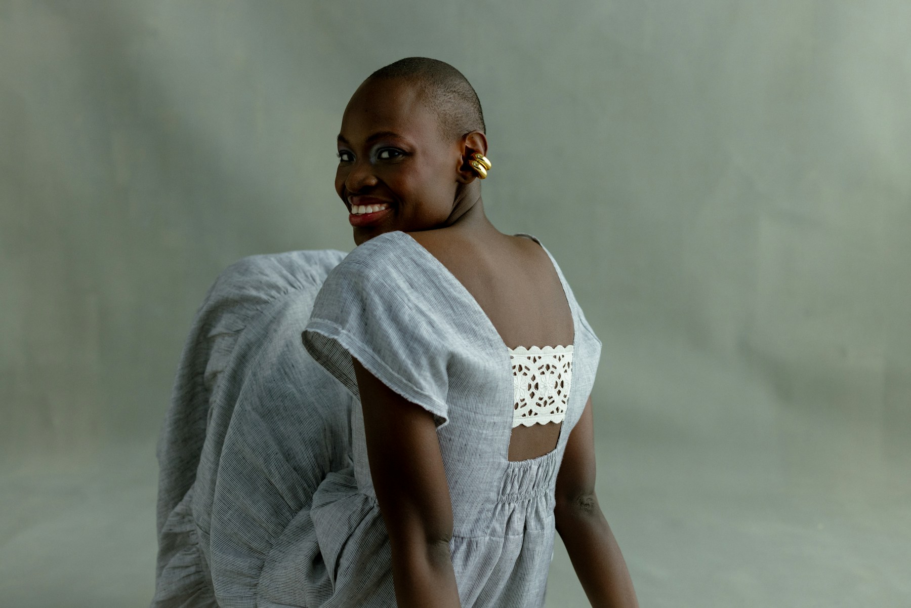 A woman wearing a neutral striped linen dress against a muted green studio background